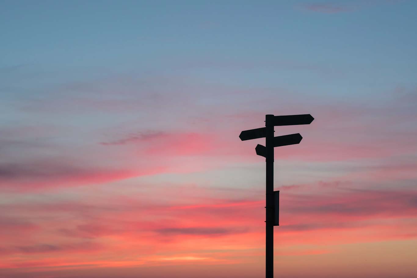 Direction sign against a sunset
